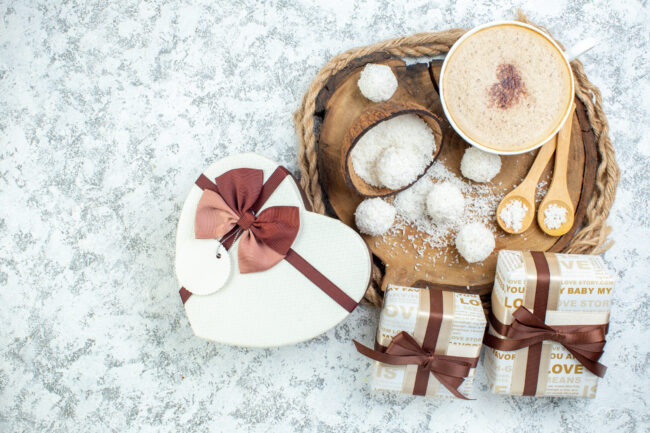 top-view-cappuccino-cup-coconut-powder-bowl-wooden-spoons-wood-board-gifts-heart-shaped-giftbox-grey-surface